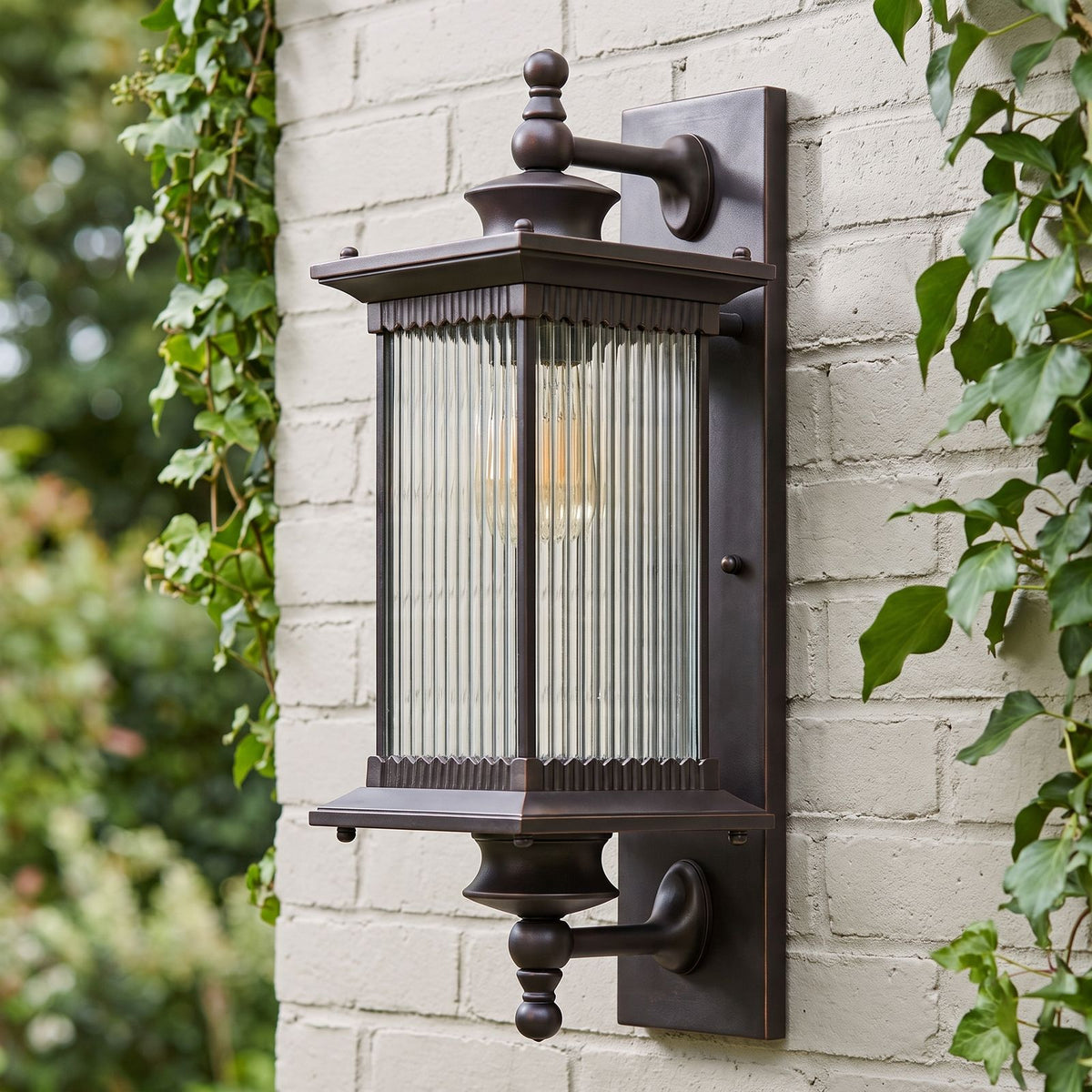Bronze Reeded Glass Outdoor Wall Lantern on a painted brick wall, angled close view
