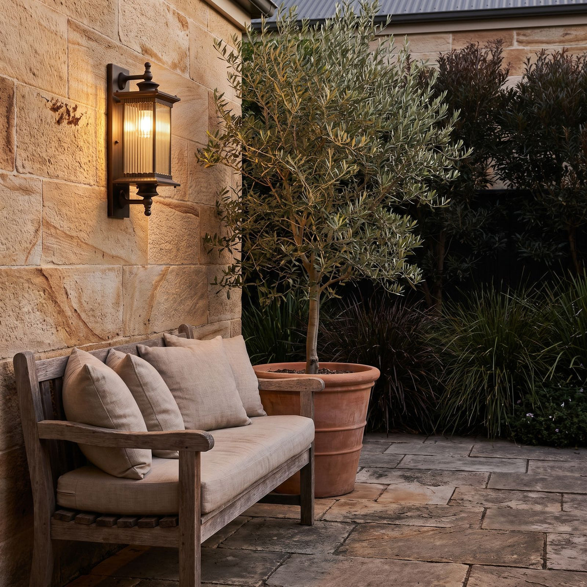 Bronze Reeded Glass Outdoor Wall Lantern on a sandstone courtyard wall above a timber bench