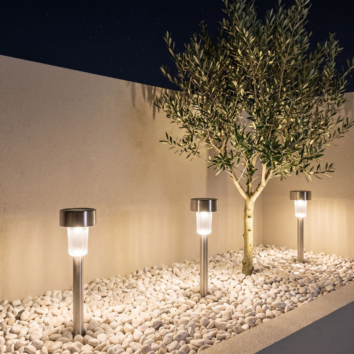 Stainless steel solar garden path light in a pebble courtyard garden at night