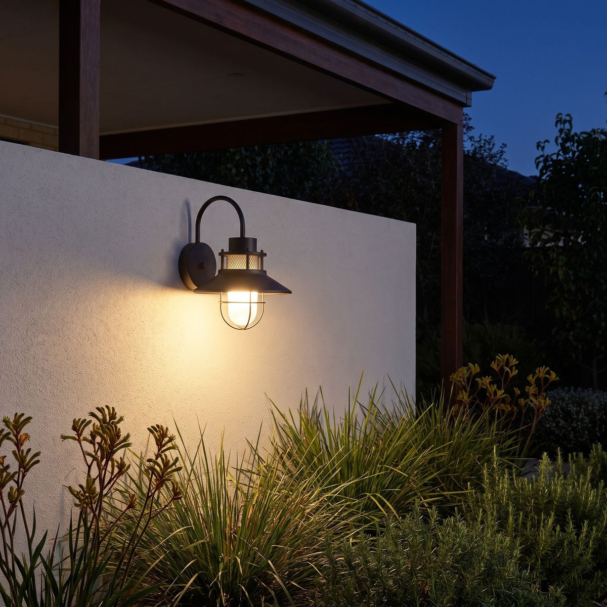 Caged frosted glass gooseneck outdoor wall light on a garden wall at night