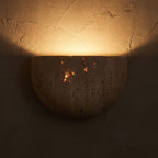 Carved Yellow Travertine Bedside Wall Light glowing on a plaster wall at night