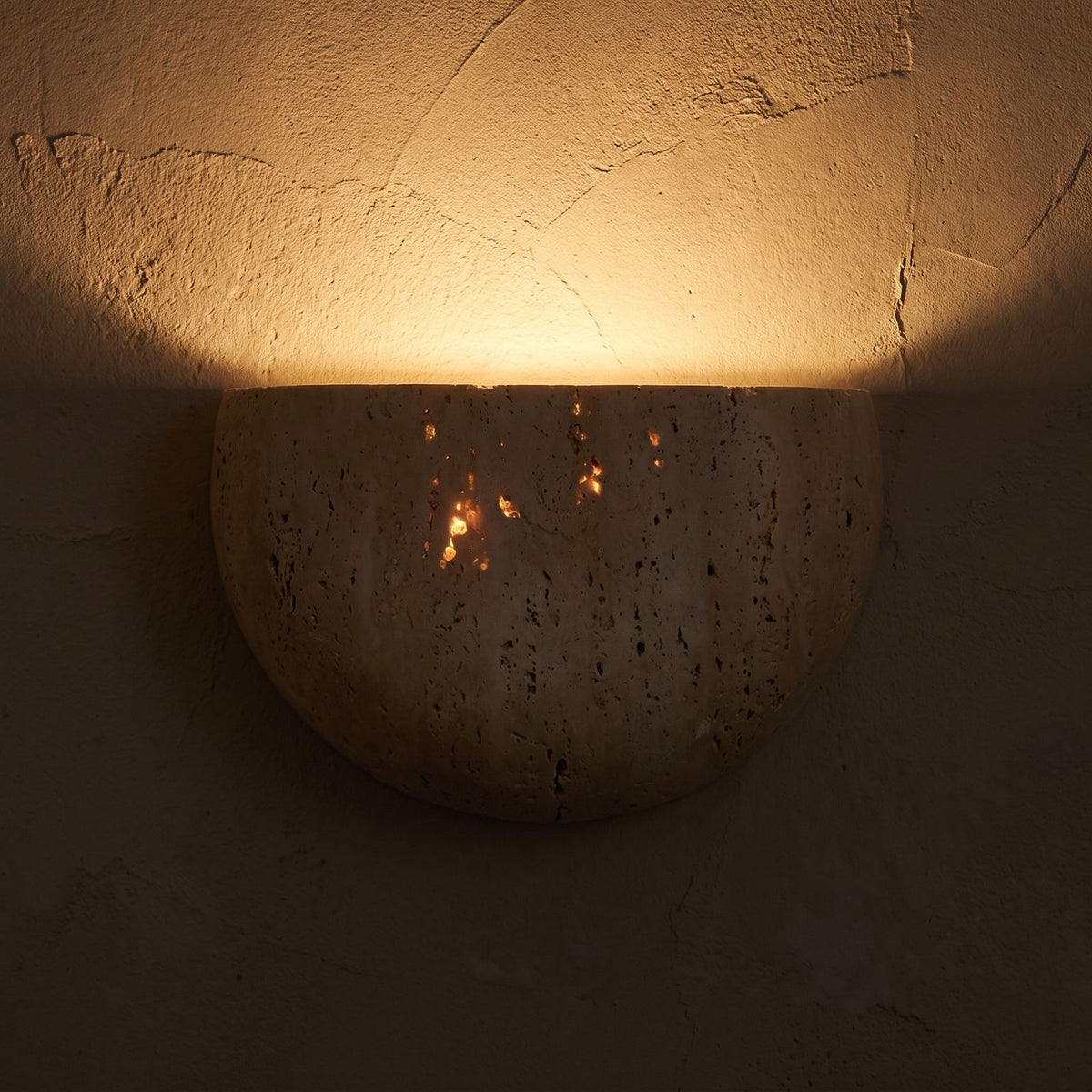 Carved Yellow Travertine Bedside Wall Light glowing on a plaster wall at night