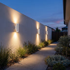 A row of Cement and Acrylic Outdoor Wall Lights along a rendered garden wall at dusk