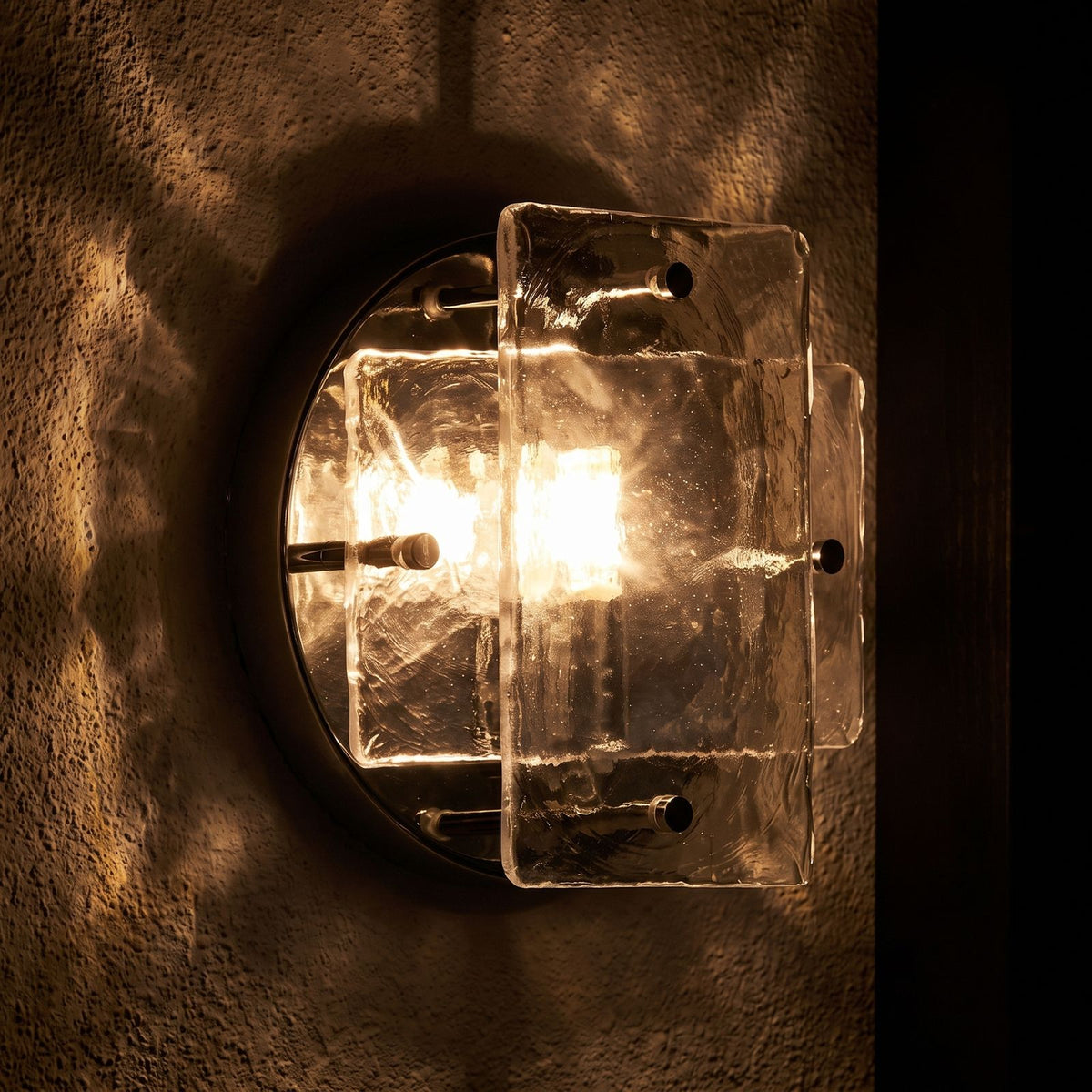 Chrome Frame Round Glass Wall Light glowing on a plaster wall at night