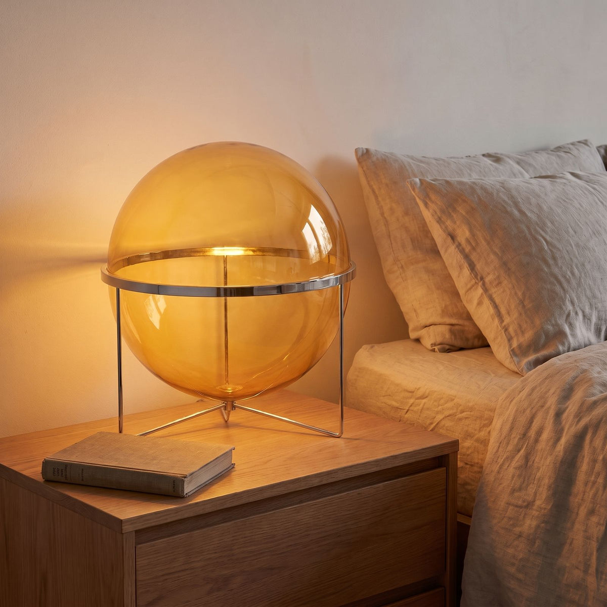 Chrome Ring Acrylic Globe Table Lamp with an amber shade on a bedside table