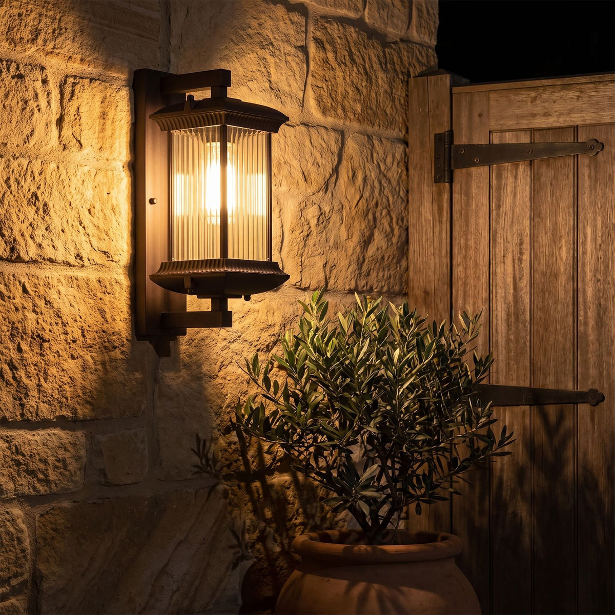 Fluted glass outdoor wall lantern on a sandstone courtyard wall at night