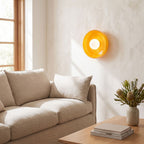 Coloured glass dish wall and ceiling light beside a living room sofa in daylight