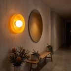 Coloured glass dish wall and ceiling light beside a round mirror in an entry hall at night