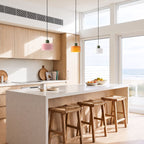 Three Colourful Two-Tone Glass Drum Pendant Lights in pink, orange and white glass in a row above a kitchen island in a beach house kitchen