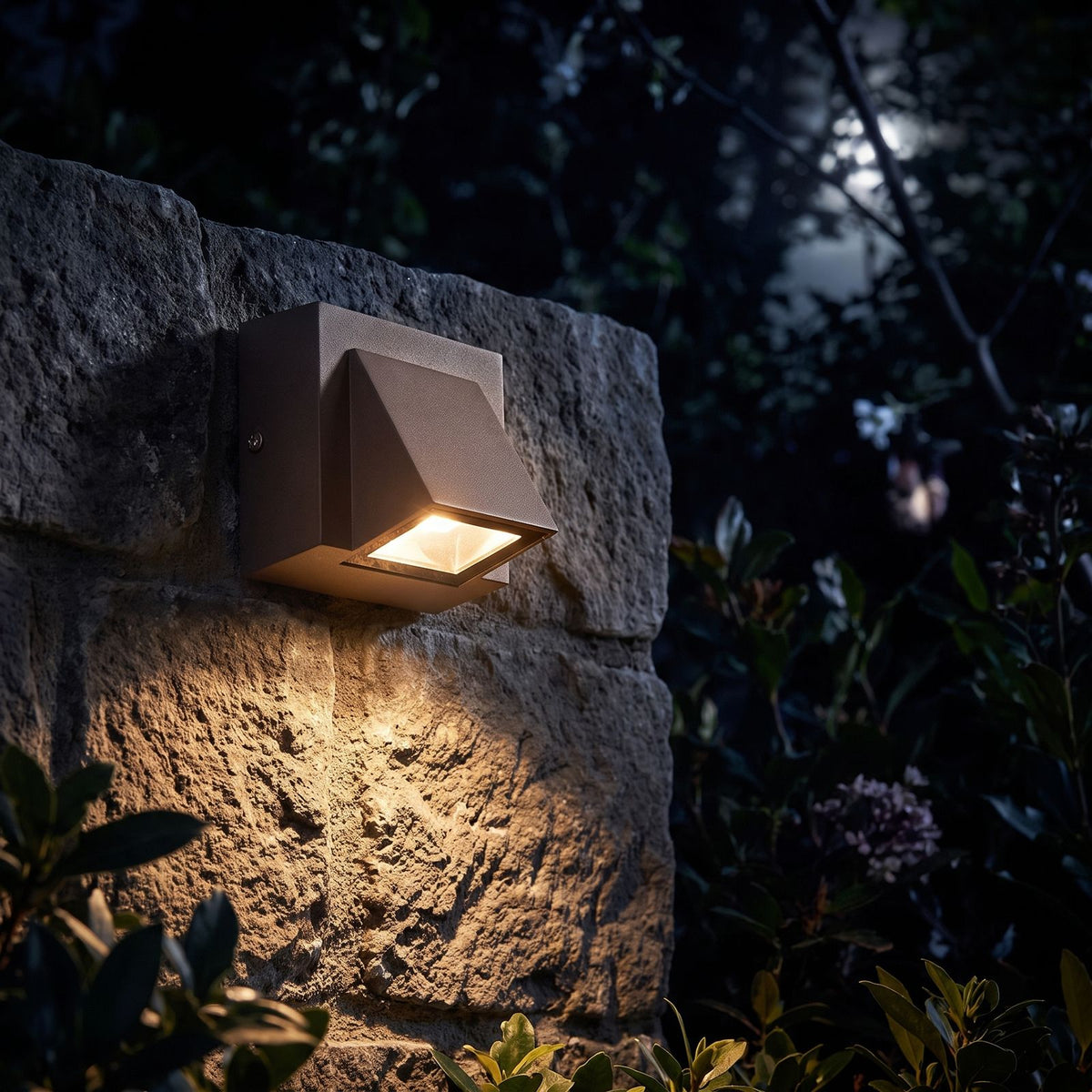 Compact Metal LED Outdoor Wall Light glowing on a garden wall at night