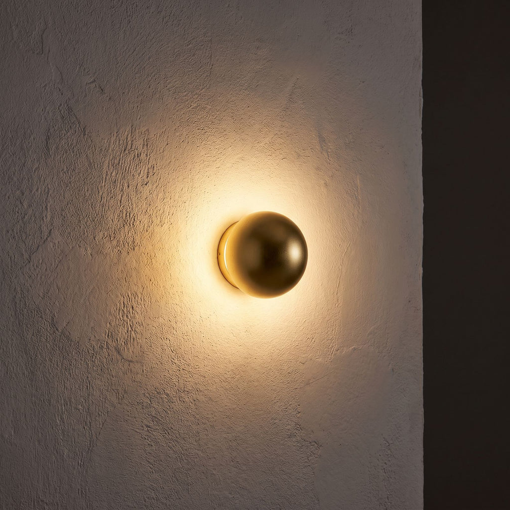 Compact Round Iron LED Wall Light glowing on a plaster wall at night