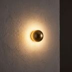 Compact Round Iron LED Wall Light glowing on a plaster wall at night