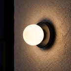 Compact Rounded Glass and Iron Wall Light glowing on a plaster wall at night