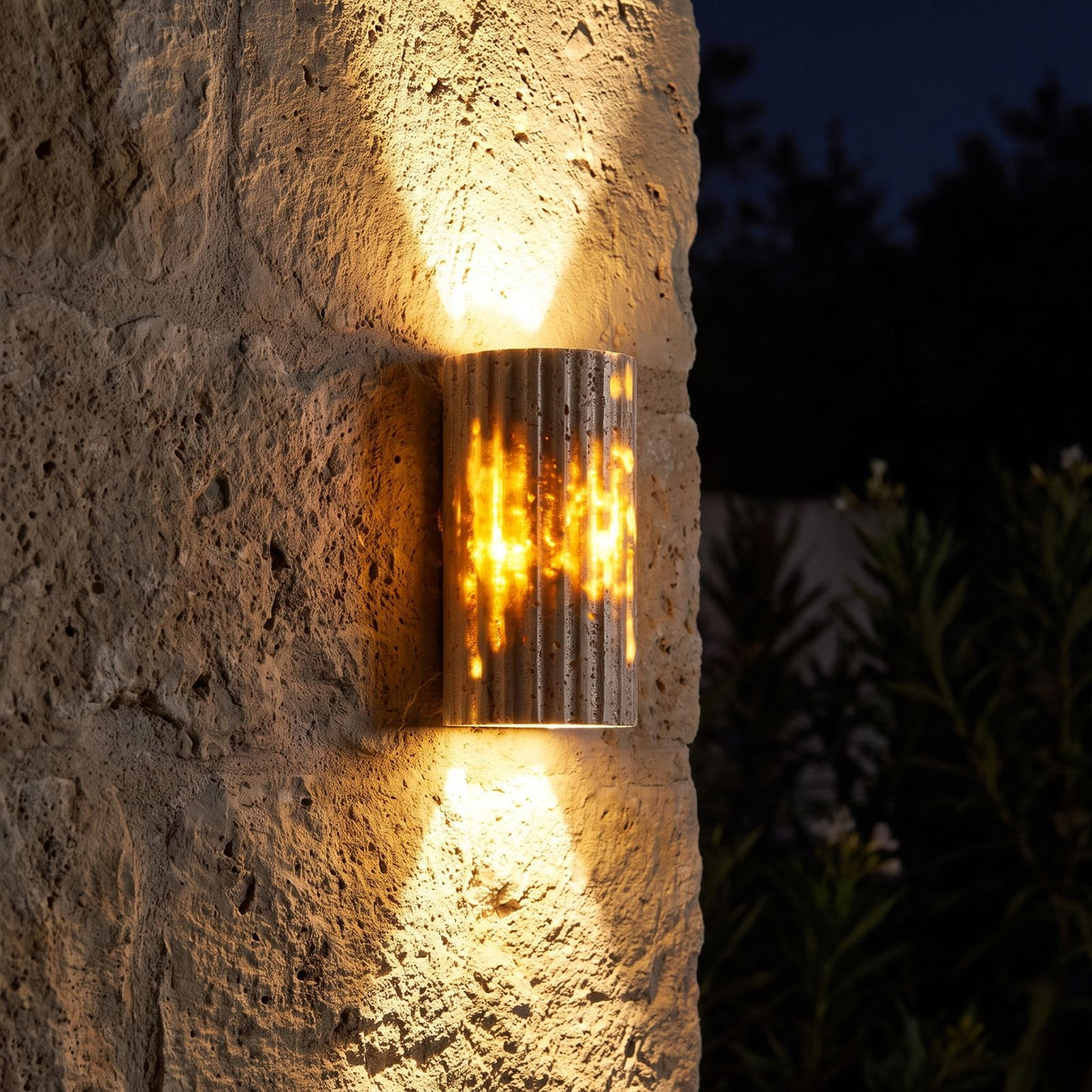 Compact Yellow Travertine Up Down Outdoor Wall Light glowing on a garden wall at night