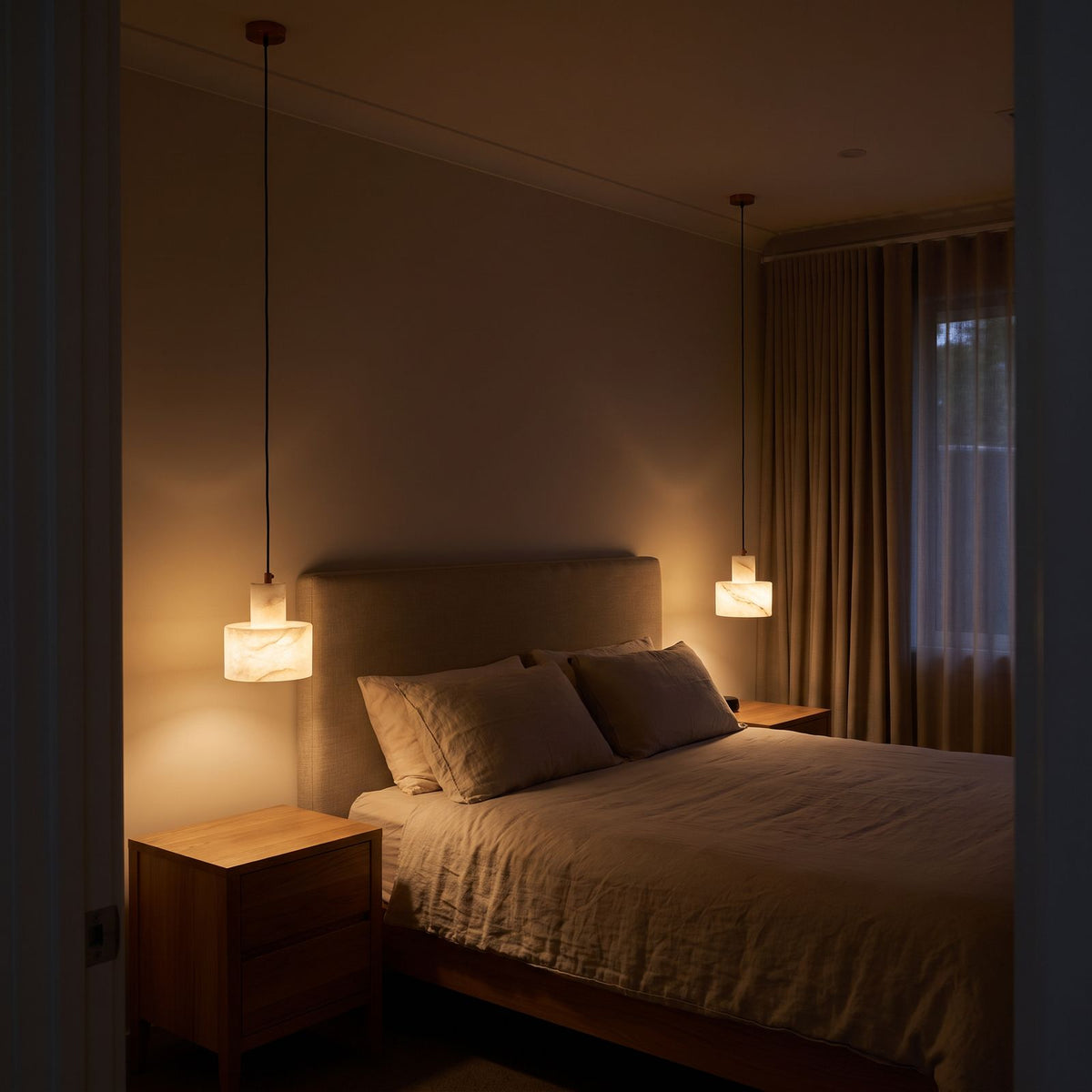 Pair of Copper and Alabaster Cylinder Pendant Lights hanging beside a bed above the bedside tables in a bedroom at night