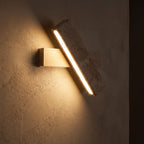 Crossed Travertine and Wood Rotating Wall Light glowing on a plaster wall at night