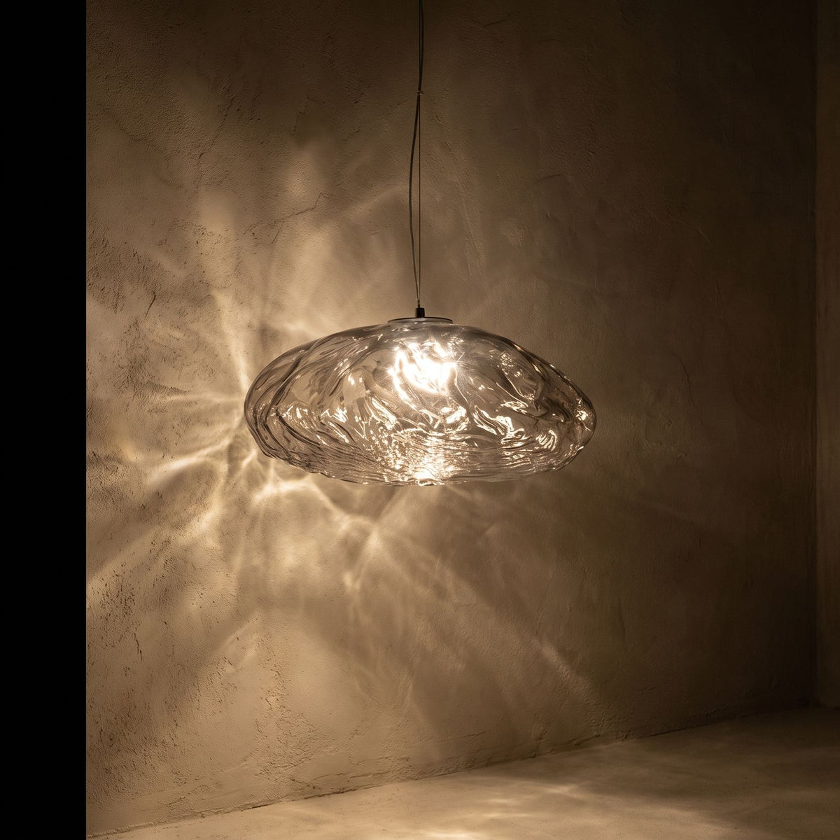 Crumpled Glass Cloud Pendant Light glowing against a plaster wall at night