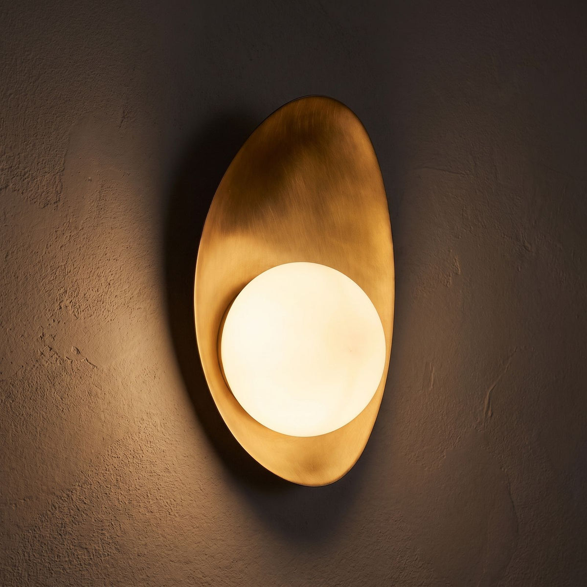 Curved Gold Shield Opal Globe Wall Light glowing on a plaster wall at night