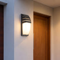 Curved Louvred Aluminium Sensor Outdoor Wall Light beside a timber front door at dusk