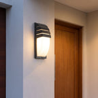 Curved Louvred Aluminium Sensor Outdoor Wall Light beside a timber front door at dusk