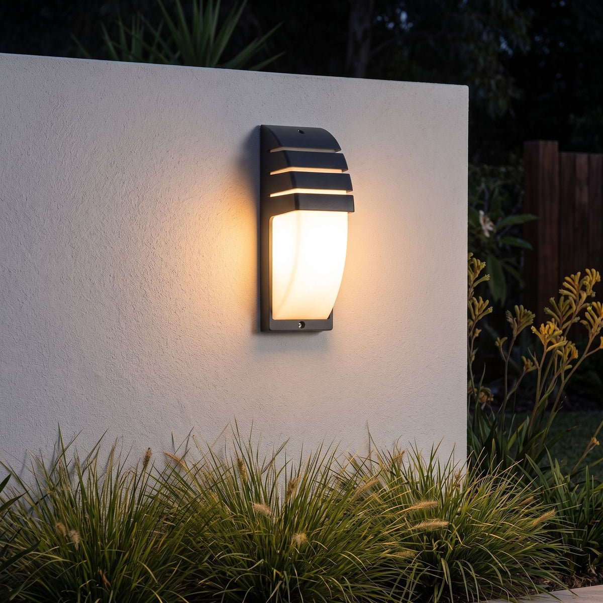 Curved louvred sensor outdoor wall light on a garden wall at night