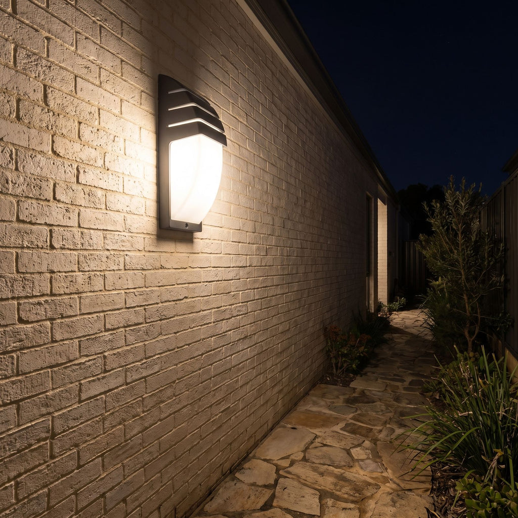 Curved louvred sensor outdoor wall light along a side passage at night