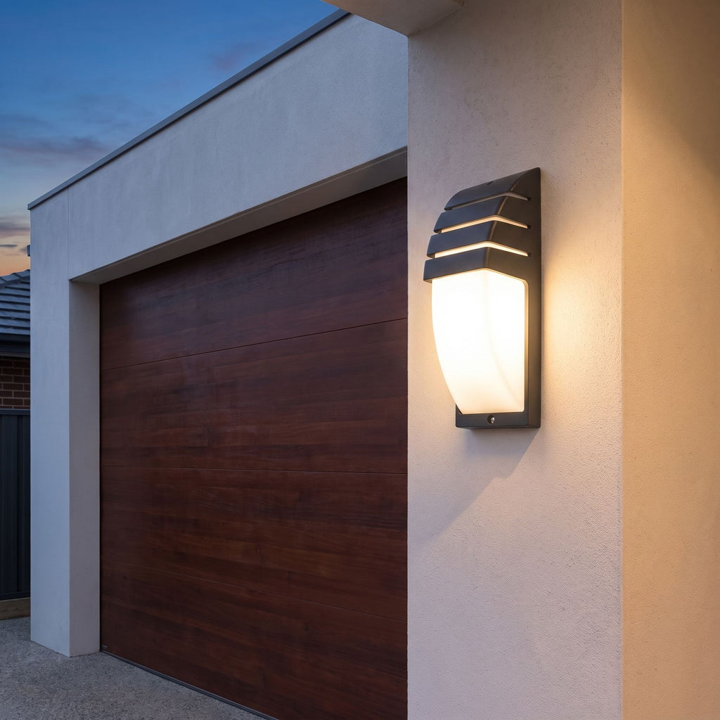 Curved louvred sensor outdoor wall light beside a garage door at dusk