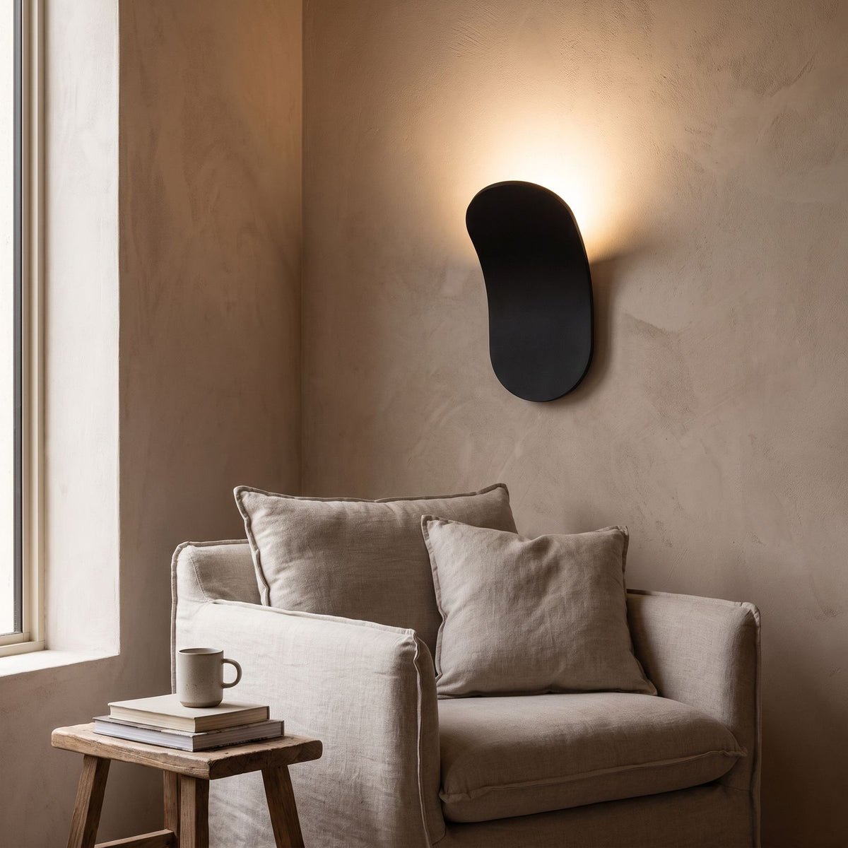Curved metal paddle indirect wall light above an armchair in a reading corner