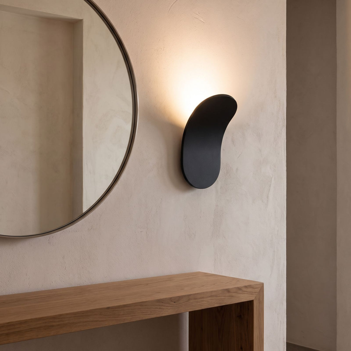 Curved metal paddle indirect wall light beside a round mirror in an entry hall