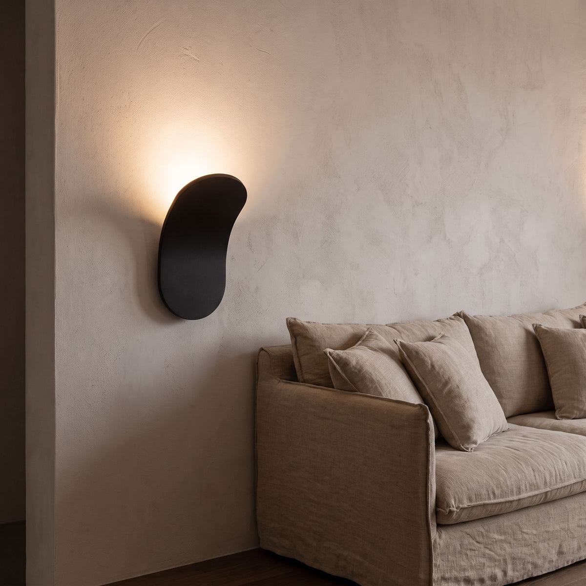 Curved metal paddle indirect wall light beside a living room sofa at night