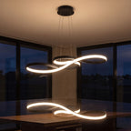 Curved ribbon aluminium LED pendant light over a dining table at night