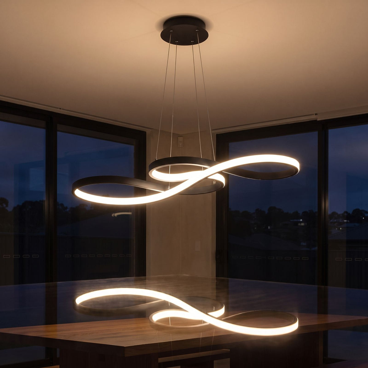 Curved ribbon aluminium LED pendant light over a dining table at night