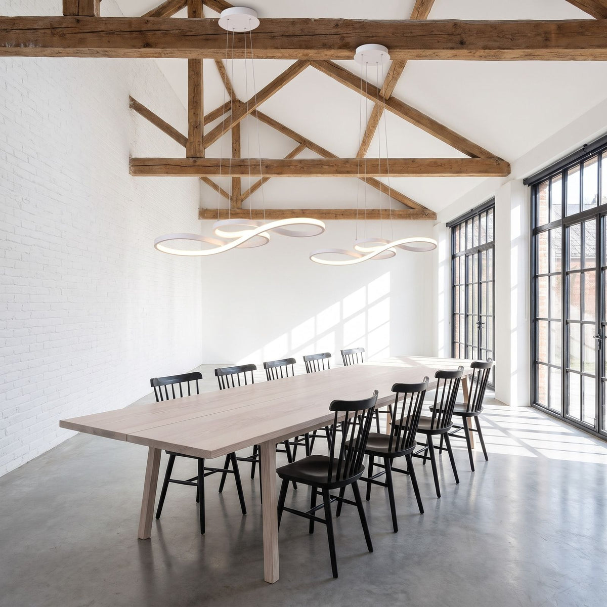 Two white Curved Ribbon Aluminium LED Pendant Lights in a row above a long dining table in a warehouse loft