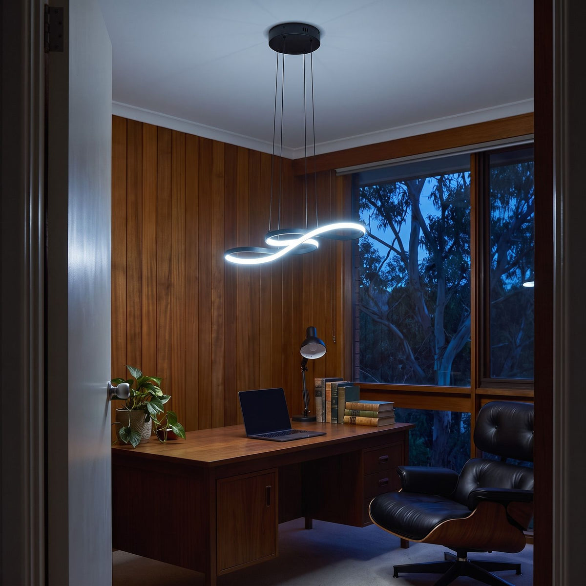 Black Curved Ribbon Aluminium LED Pendant Light in cool white above a home office desk in a timber-panelled study at dusk
