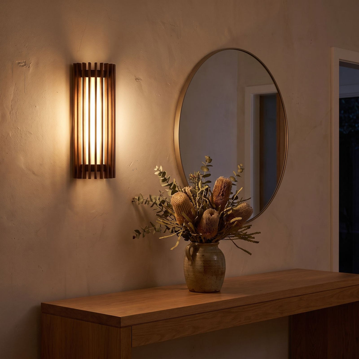 Curved slatted wood wall sconce beside a round mirror in an entry hall