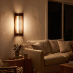 Curved slatted wood wall sconce beside a living room sofa at night