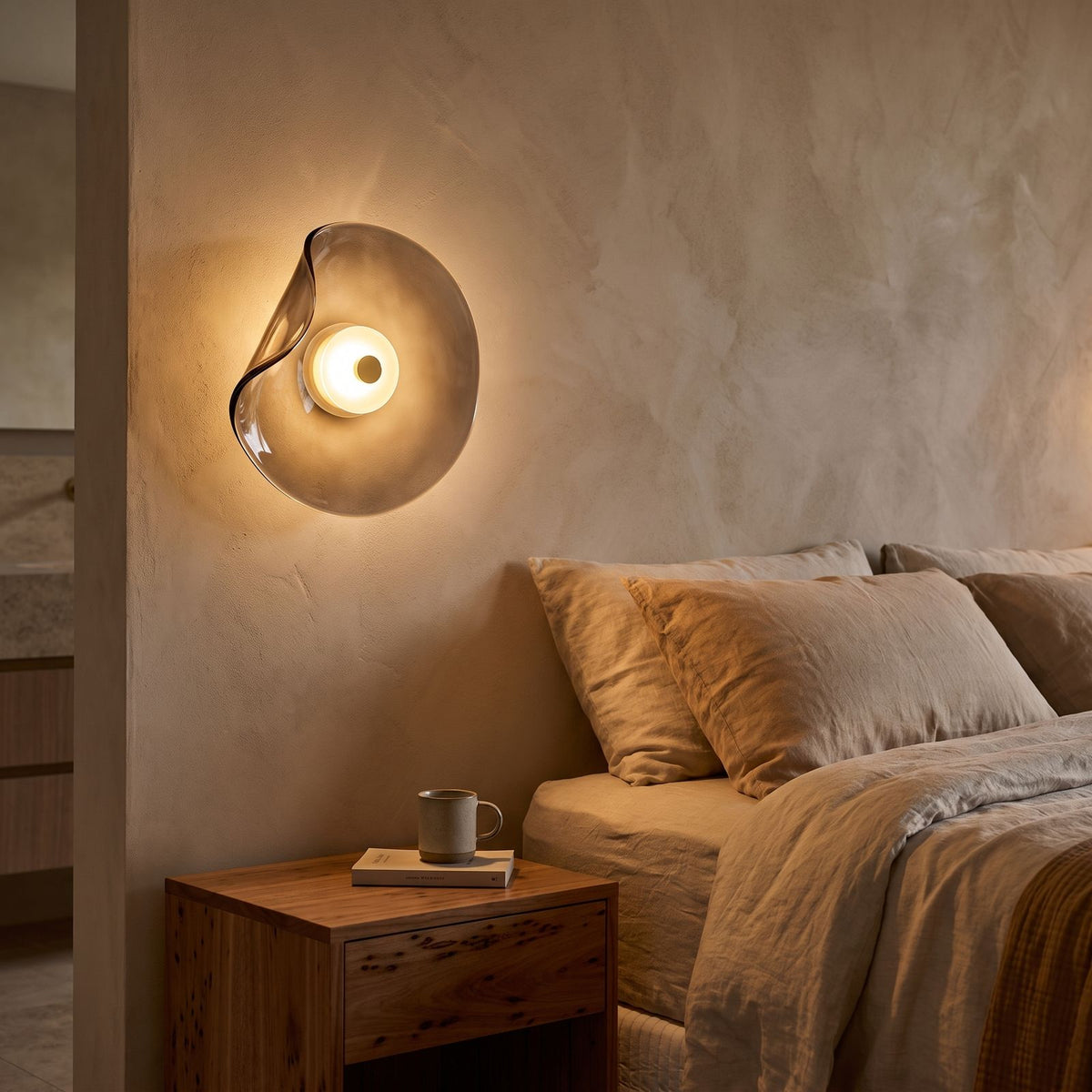 Curved Smoke Glass Up Down Wall Light beside a bed with linen bedding
