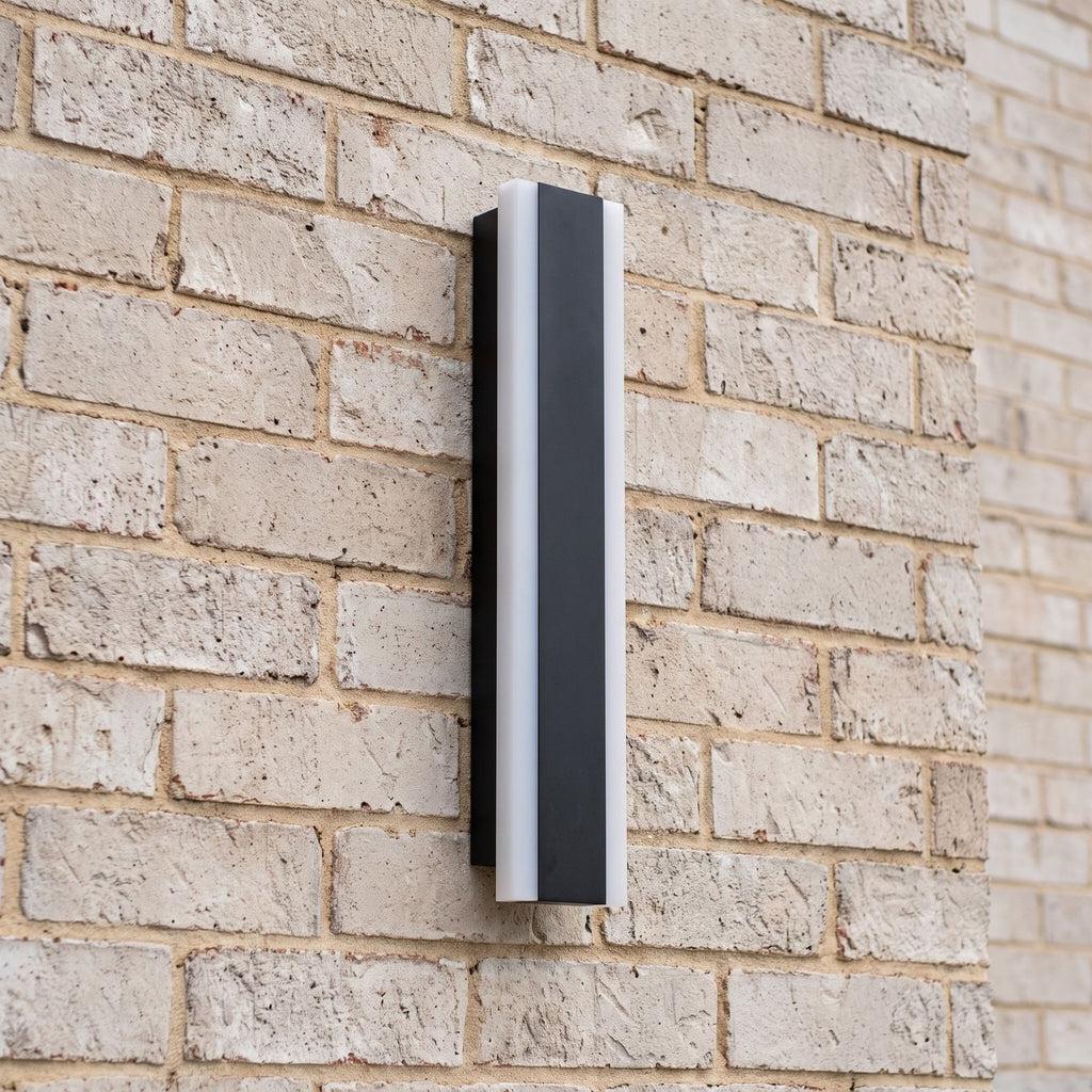Side view of a slim black linear wall light mounted on a pale face brick wall in daylight