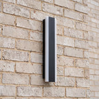 Side view of a slim black linear wall light mounted on a pale face brick wall in daylight