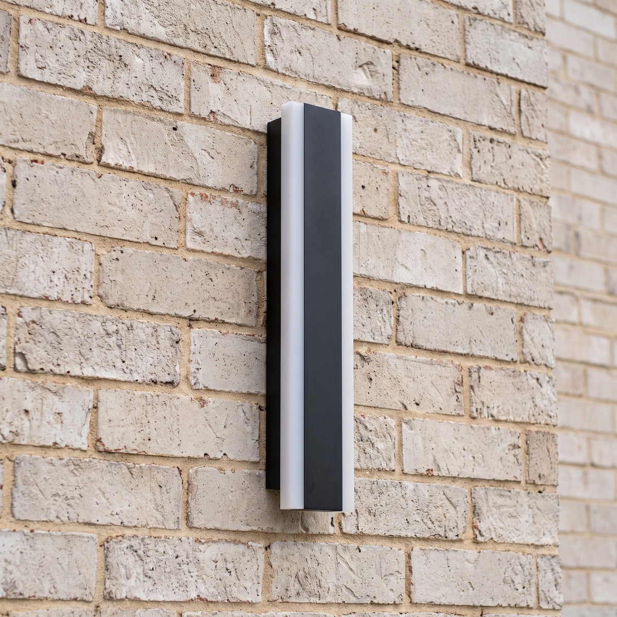 Side view of a slim black linear wall light mounted on a pale face brick wall in daylight