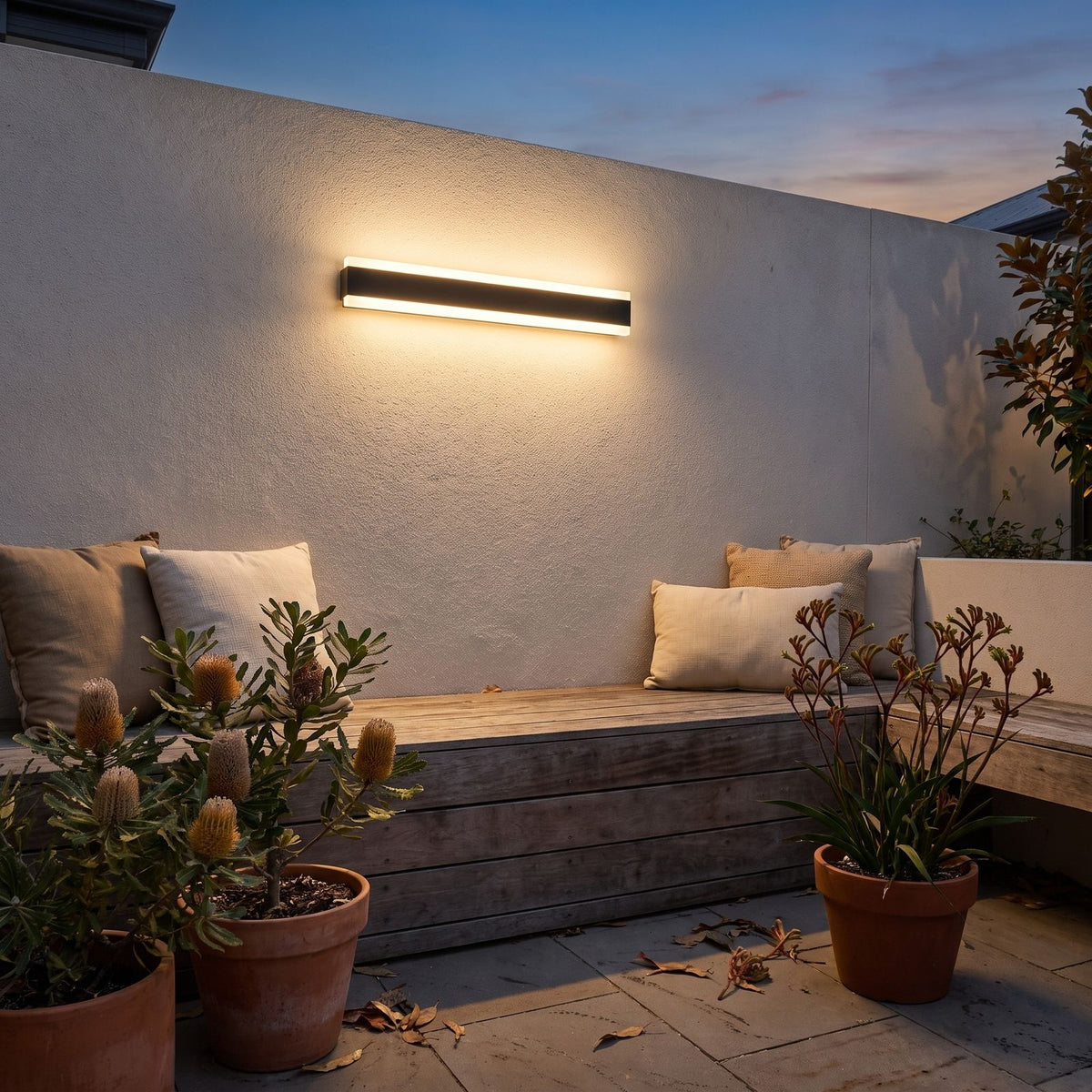 Linear LED wall light mounted horizontally above a timber bench in a courtyard at dusk