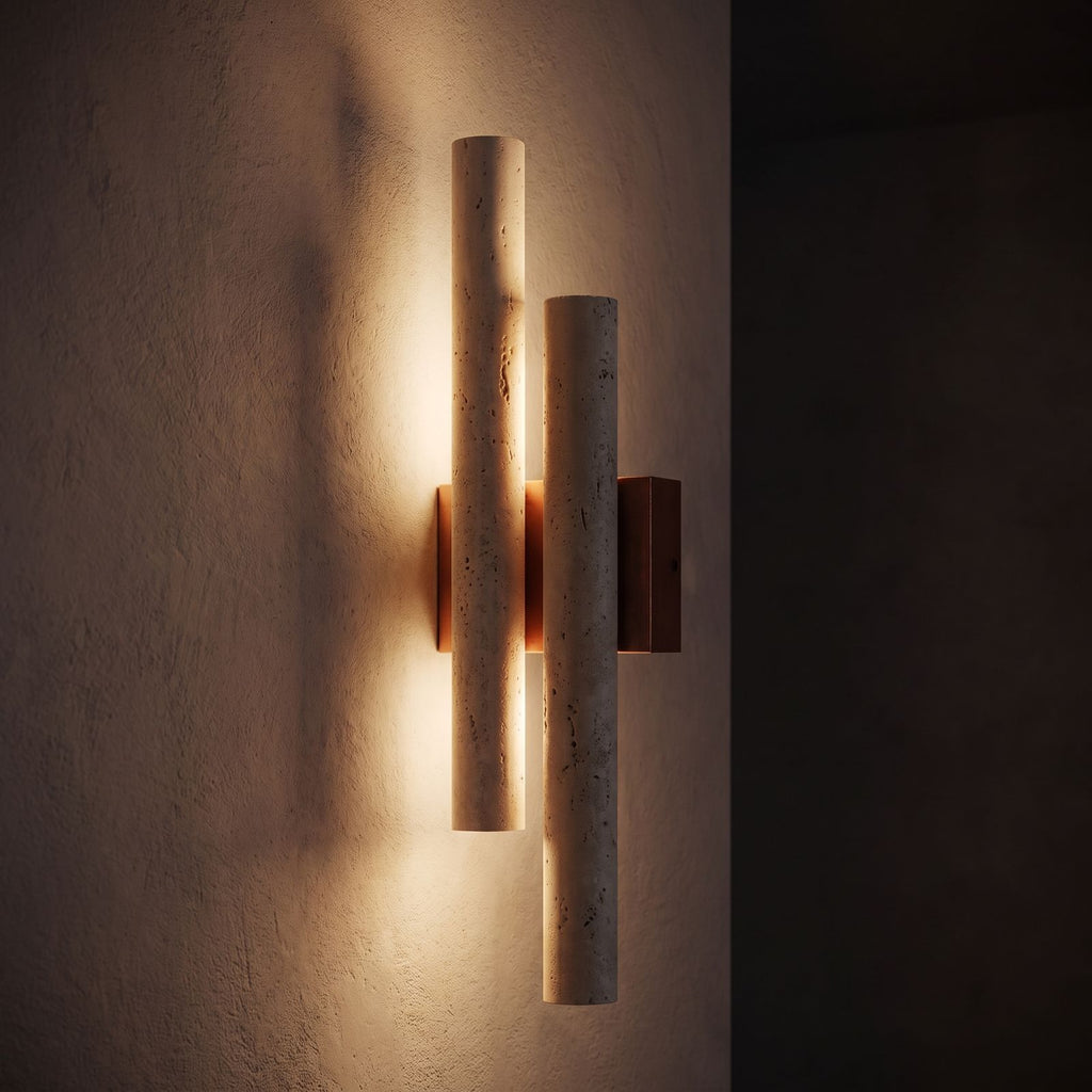 Double Travertine Column Wall Light glowing on a plaster wall at night