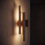 Double Travertine Column Wall Light glowing on a plaster wall at night