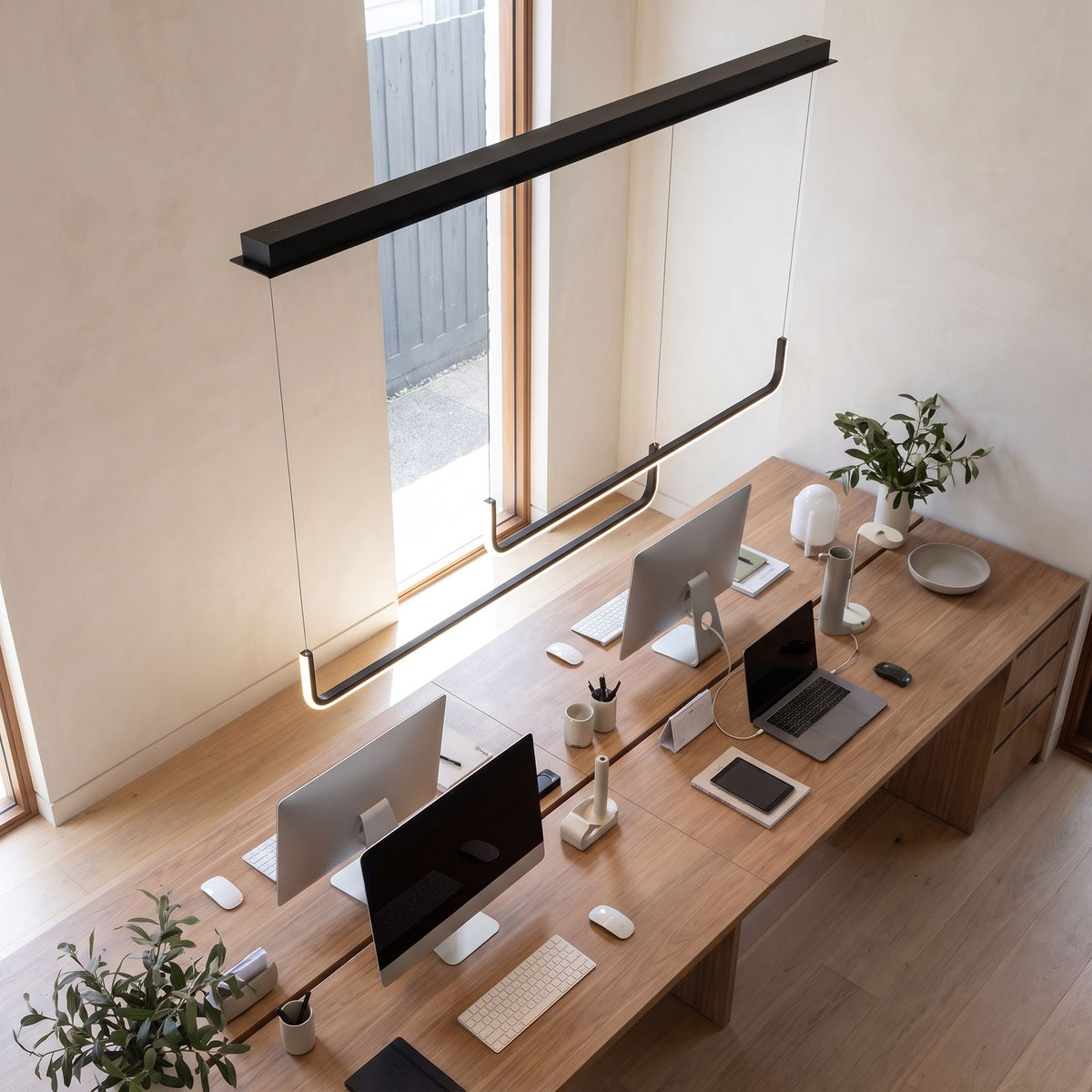 Double U-bar linear LED pendant light above a home office desk in daylight