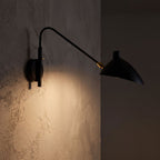 Duckbill Shade Adjustable Arm Wall Light glowing on a plaster wall at night