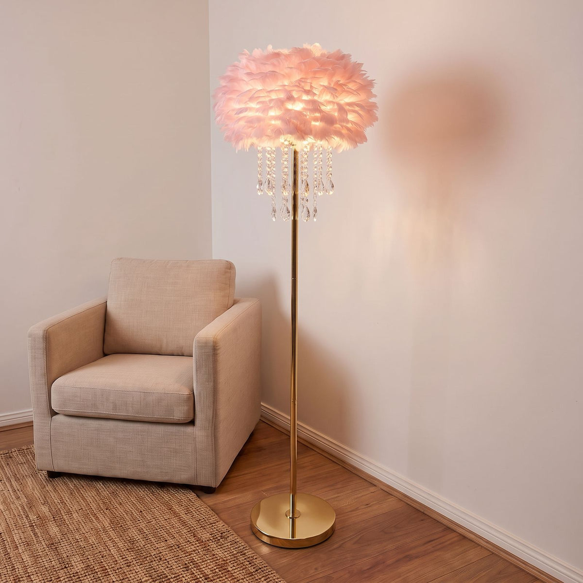 Feather Shade Crystal Drop LED Floor Lamp with a pink shade and brass finish body beside an armchair in a living room corner
