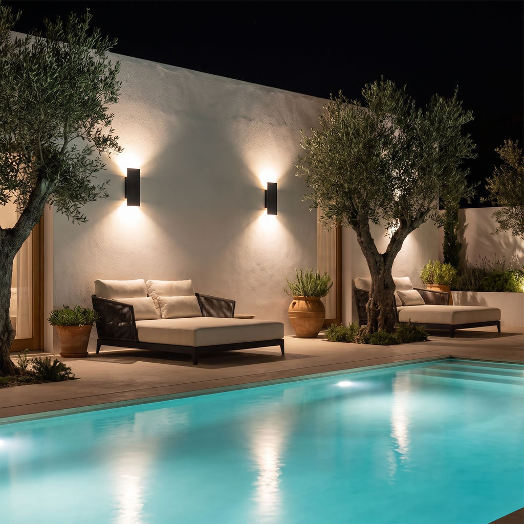 Two Flat Bar Aluminium Up Down Outdoor Wall Lights in black on a courtyard wall beside a pool at night