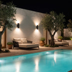 Two Flat Bar Aluminium Up Down Outdoor Wall Lights in black on a courtyard wall beside a pool at night