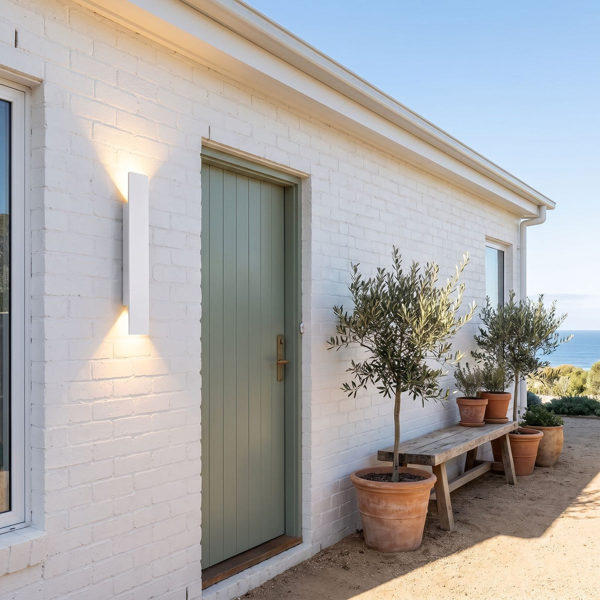Flat Bar Aluminium Up Down Outdoor Wall Light in white beside the green front door of a white brick coastal house