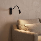 Flexible gooseneck reading wall light beside a living room sofa at night